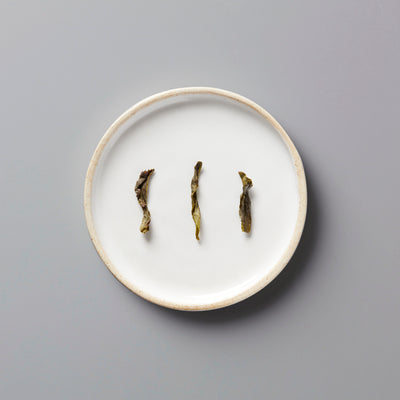 Lins Big Leaf dancong oolong tea leaves displayed on white ceramic plate showcasing twisted dark leaf shape