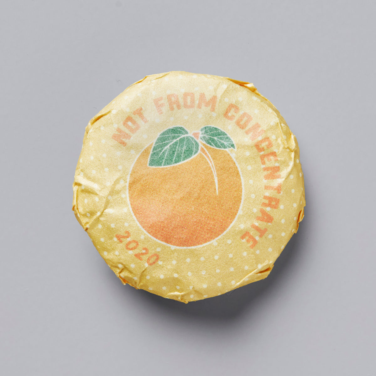 2020 Not From Concentrate white tea cake with peach illustration on yellow wrapped paper against grey background