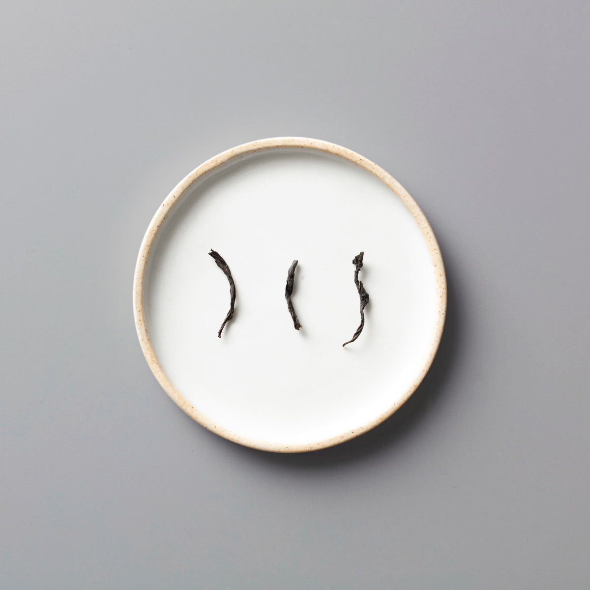 Three twisted Panlan Que She yancha oolong tea leaves arranged on a minimalist white ceramic plate