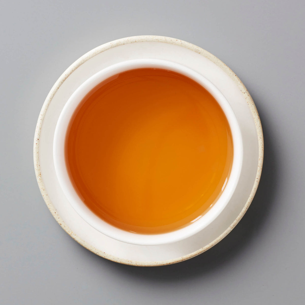 Champagne Long Kou oolong tea with amber-colored liquor in white ceramic cup on grey background
