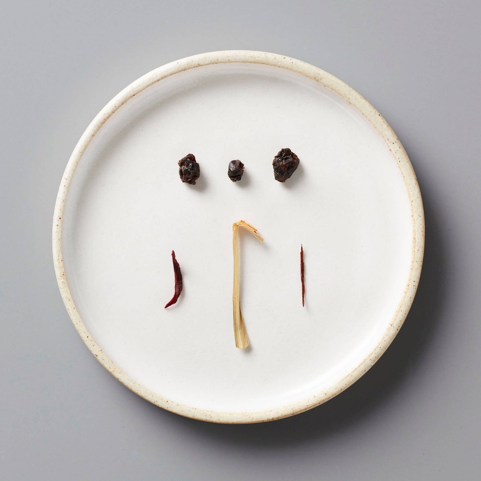 CURRANT tisane blend ingredients artfully arranged on white ceramic plate showing dried currants and herbs