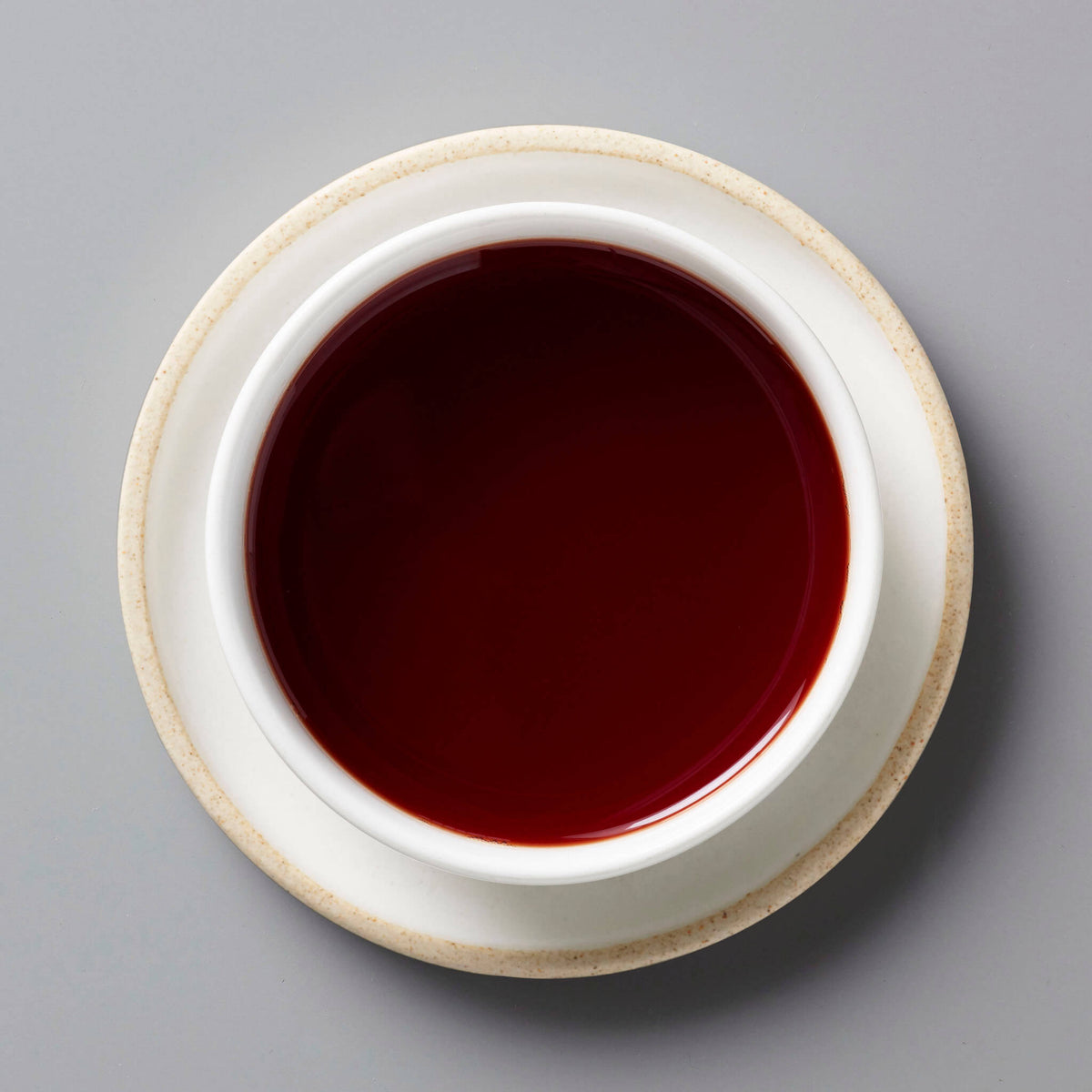 CURRANT tisane blend steeped to a deep ruby red color in white ceramic cup on light saucer against grey background