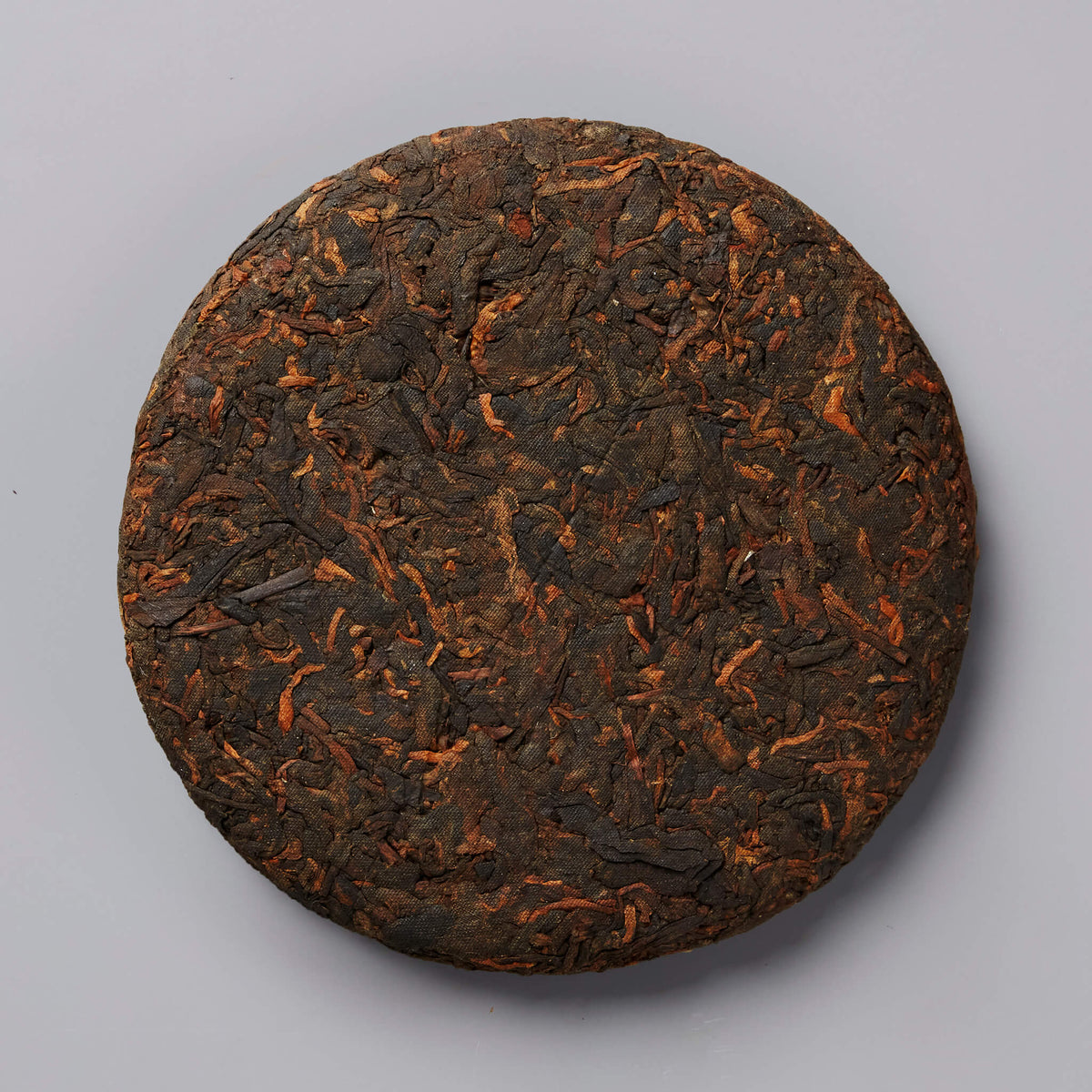 Compressed disc of 2020 DIGESTIF shou puer tea with dark brown and reddish leaf texture on gray background