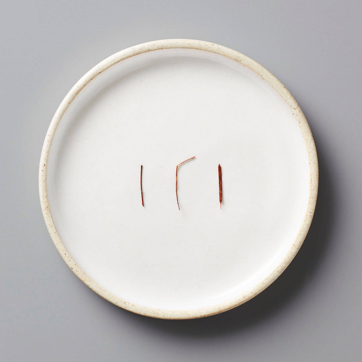 FYN ROOIBOS tisane needles displayed on white ceramic plate with raised rim against grey background