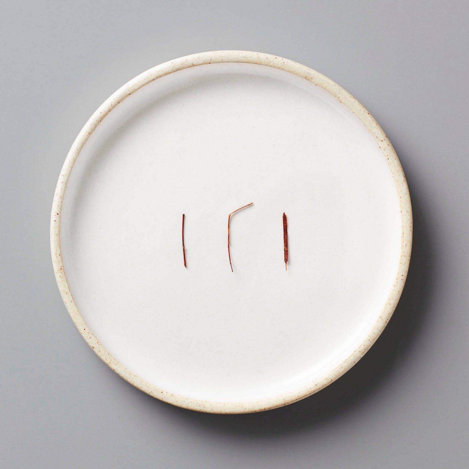 FYN ROOIBOS tisane needles displayed on white ceramic plate with raised rim against grey background