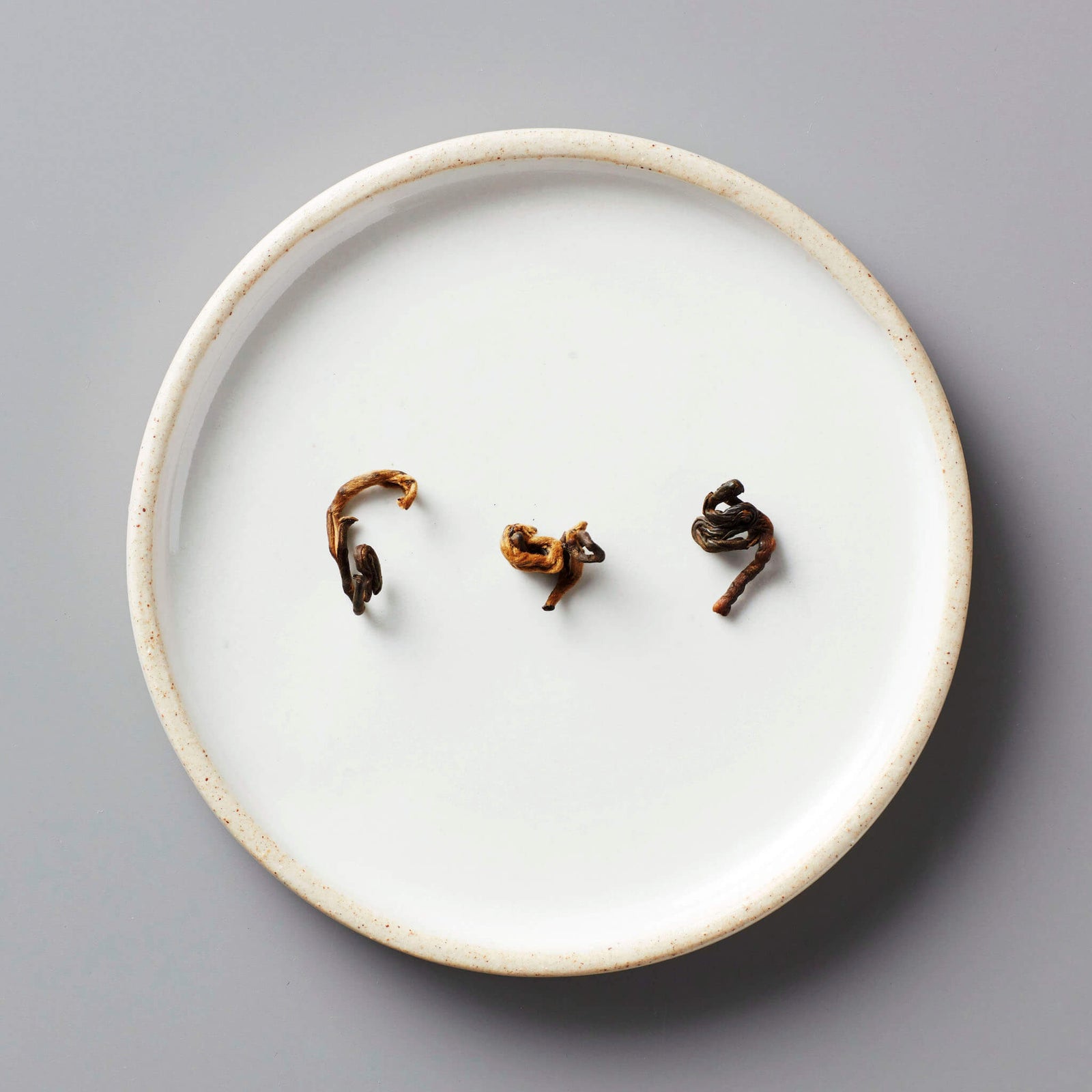 HUGO GREY black blend tea leaves artfully arranged on white ceramic plate showing natural curl and texture
