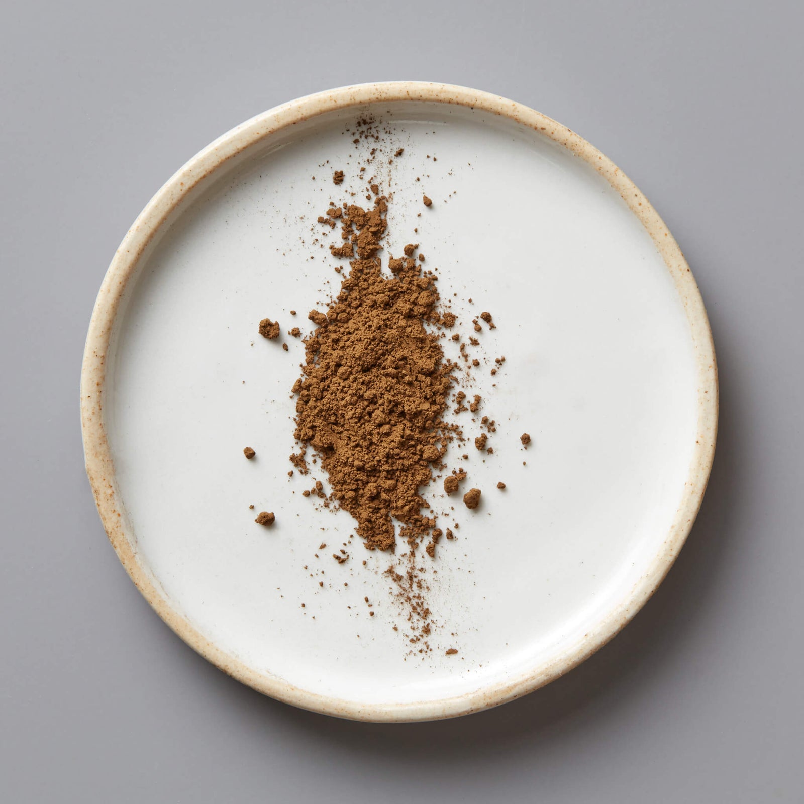 HOUJI POWDER HUGO green tea powder scattered on white ceramic plate with beige rim