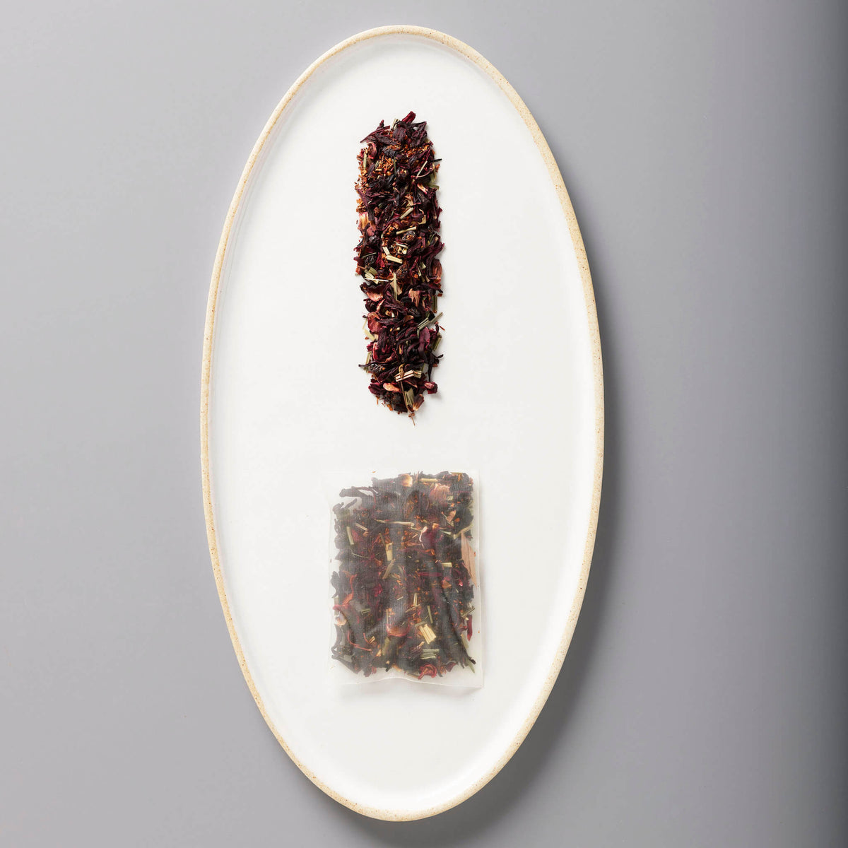 Iced Hibiscus Berry loose leaf blend and tea bag on white oval plate showing deep purple-red organic tisane mix