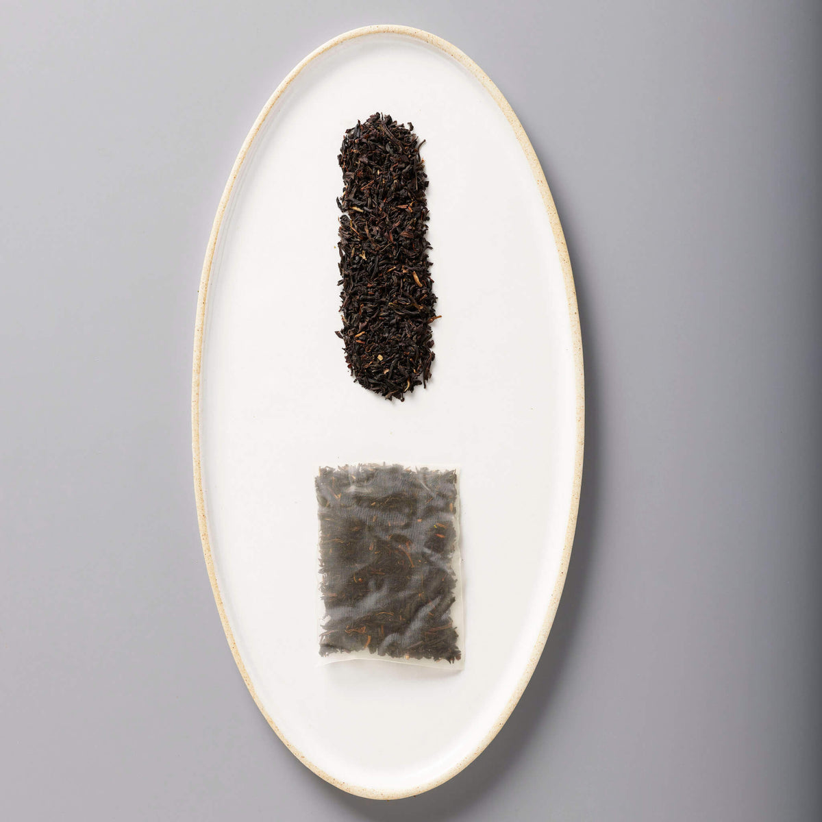 Iced Mango Black tea leaves and sachet on white oval plate showing loose and packaged tea forms