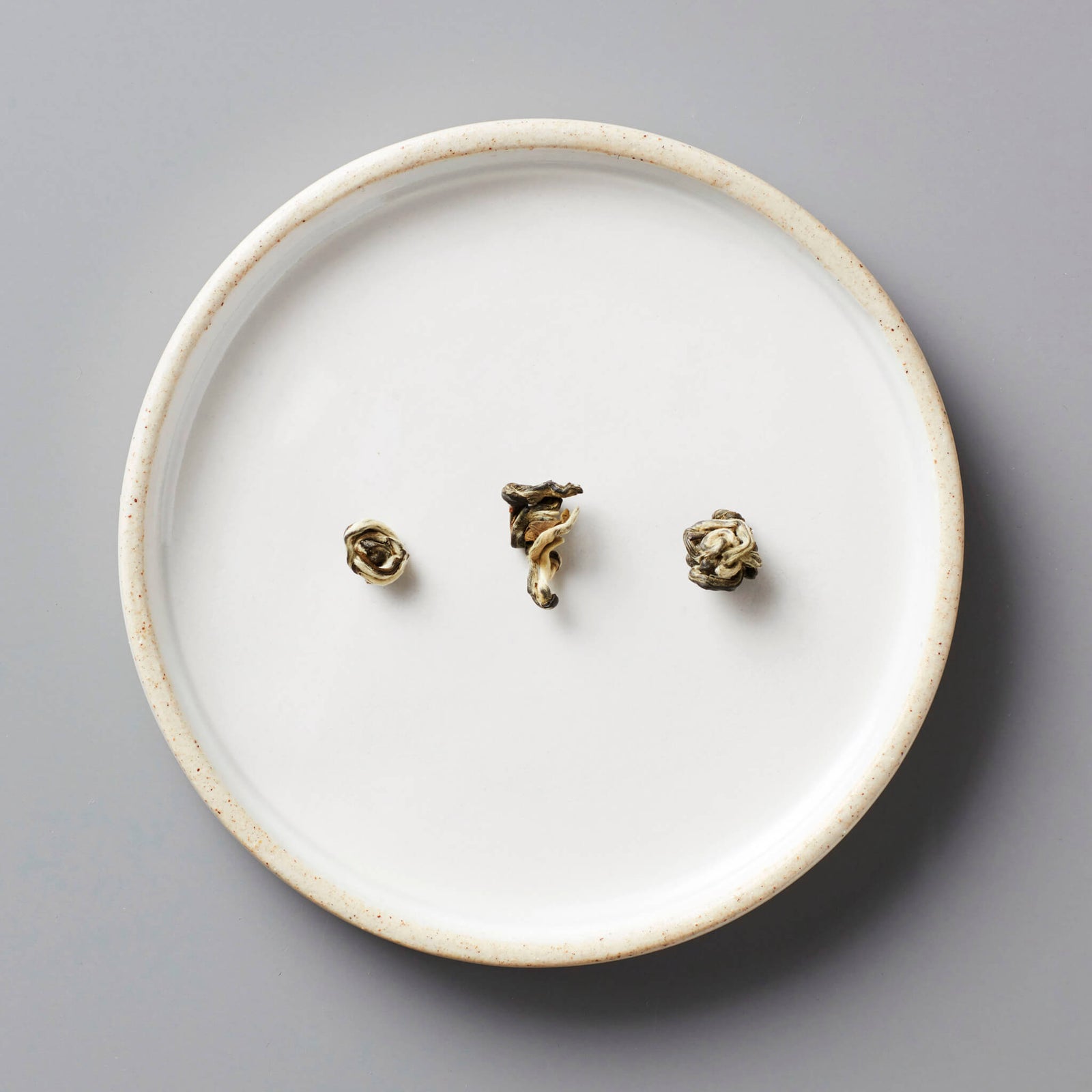 Jasmine Bai Hao scented green tea pearls on white ceramic plate showing delicate rolled leaves for steeping