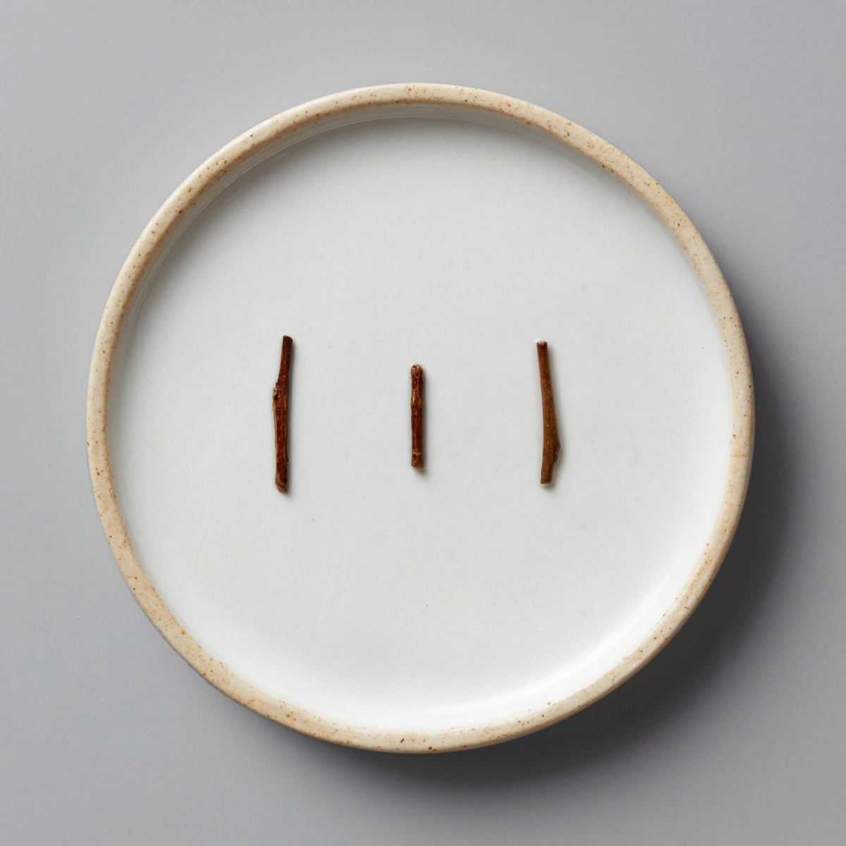 KABUSE HOUJICHA green tea stems displayed on a white ceramic plate with textured rim against grey background