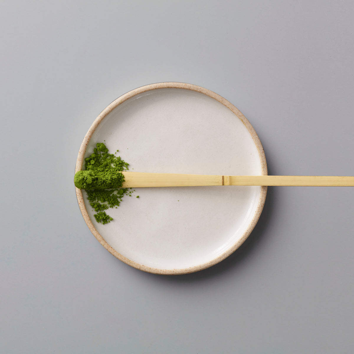 Matcha Scoop Chashaku bamboo tea scoop with green matcha powder on white ceramic plate against grey background