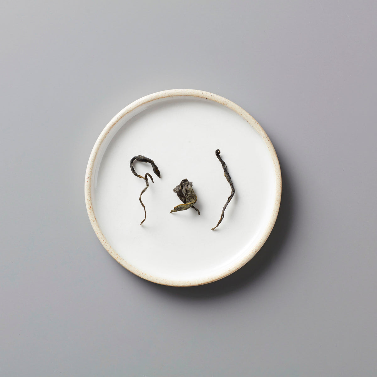 Long Kou Maofeng green tea leaves displayed on white ceramic plate showing delicate twisted dry leaf form