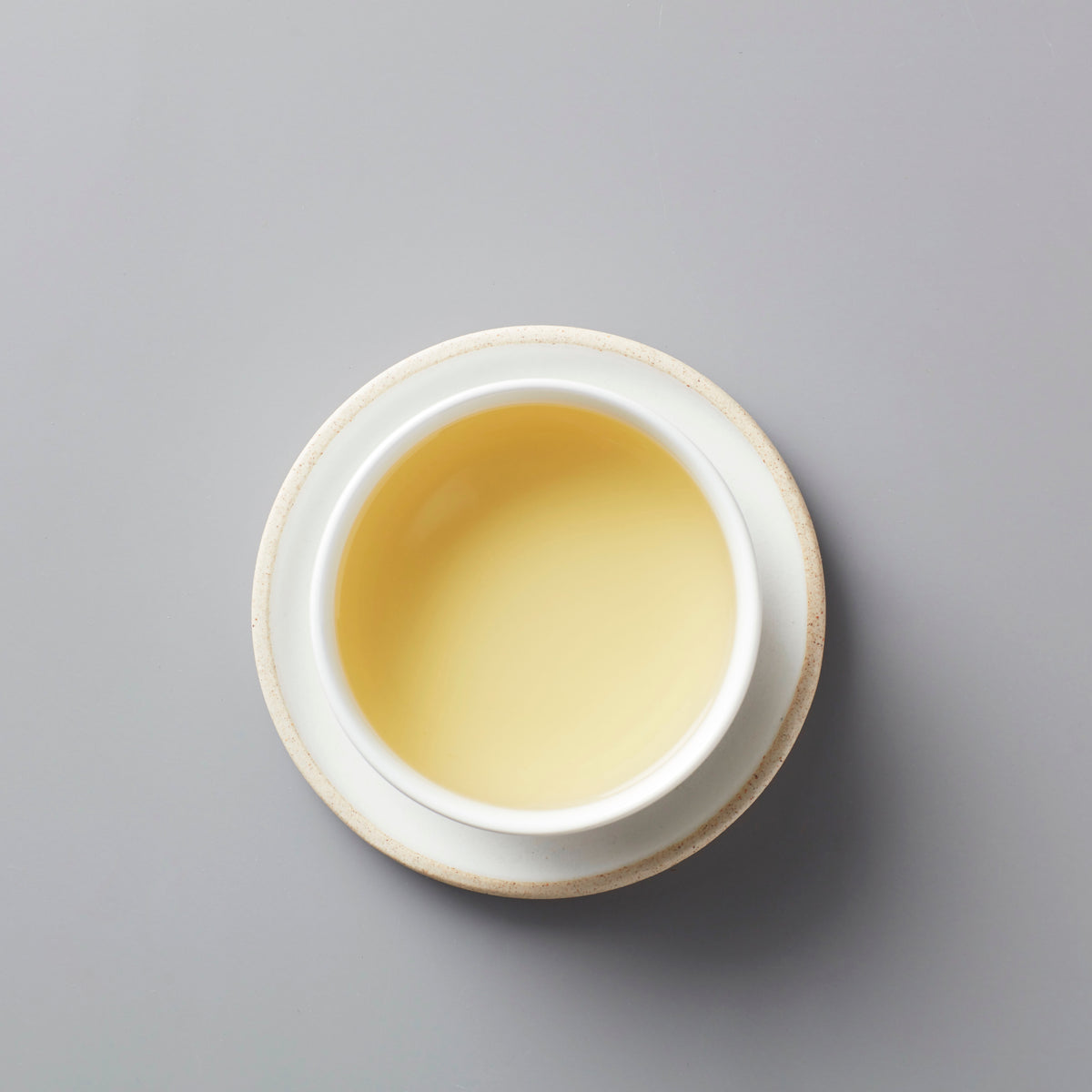 Long Kou Maofeng green tea in white ceramic cup showing pale yellow-green liquor against grey background