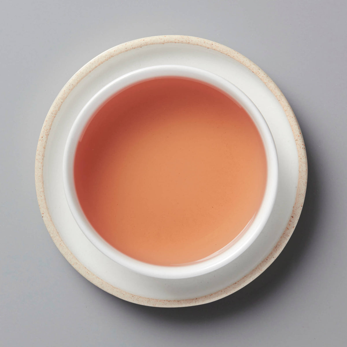 ROSE tisane steeped to a vibrant pink color in white ceramic cup, top-down view on grey background