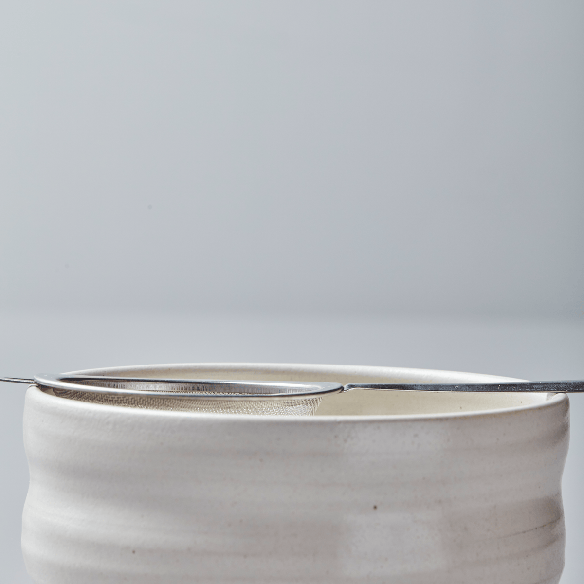 Stainless steel Matcha Sifter resting on white ceramic bowl, featuring fine mesh for smooth matcha powder preparation