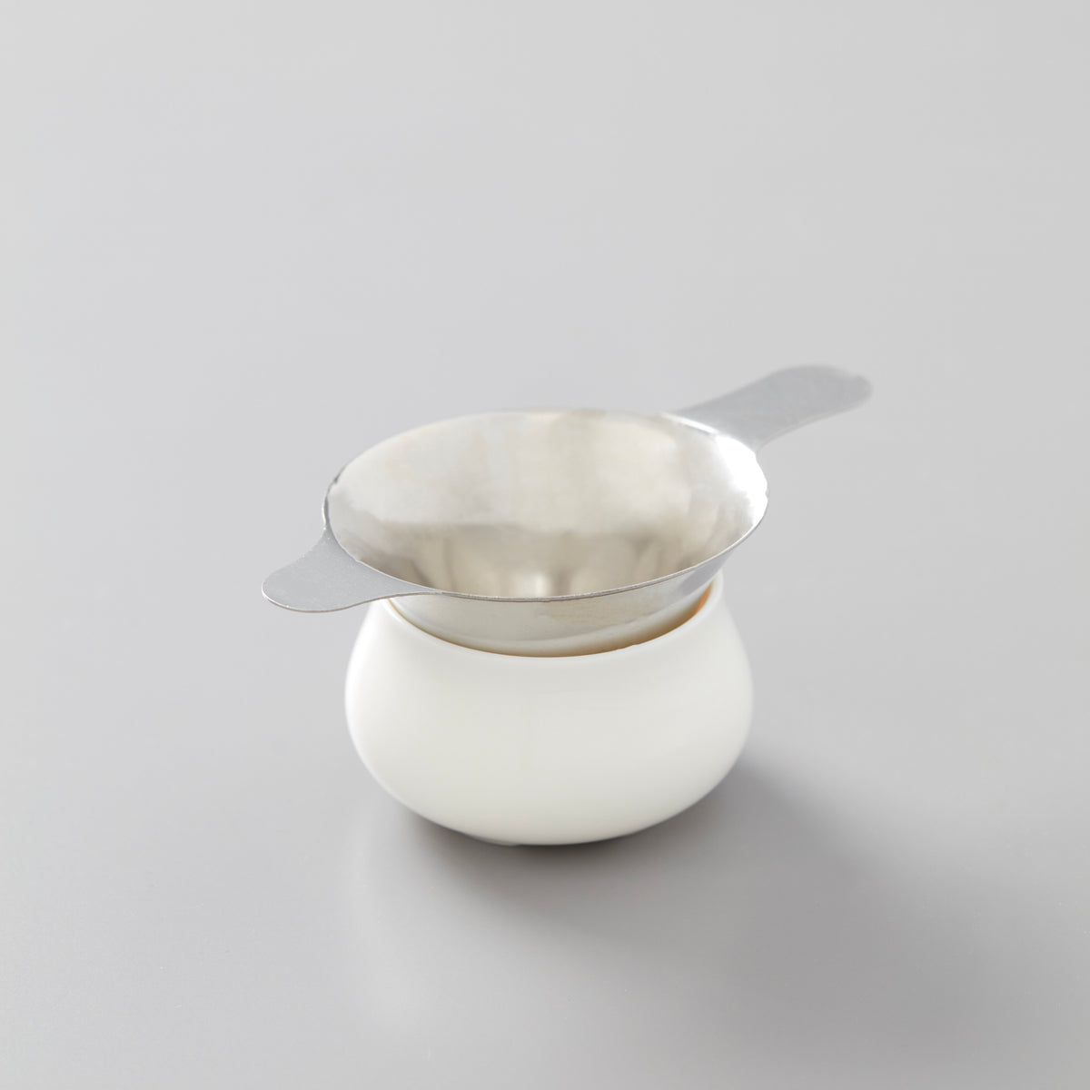 Steel filter resting on white ceramic vessel, designed for straining tea leaves during traditional gongfu tea preparation